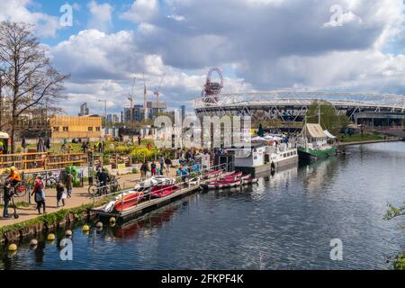 LONDON, Großbritannien - 11. APRIL 2021: Menschen vor den Grachtenbars in Hackney Wick in London an einem sonnigen Tag. Im Hintergrund sieht man das West Ham Stadium. Stockfoto