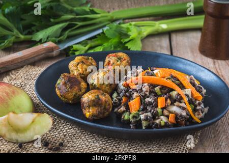 Gebratene Gemüsebällchen mit Linsensalat auf schwarzem Teller auf Holztisch, veganes Food-Konzept Stockfoto