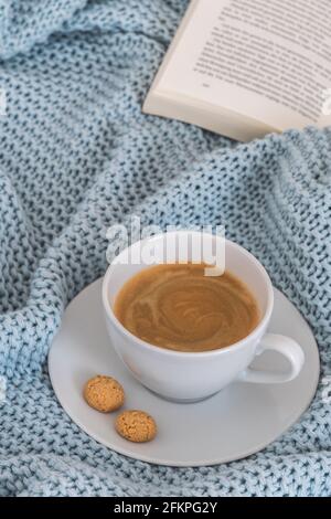 Tasse Kaffee auf einer hellblauen Strickdecke aus Wolle. Gemütliche Atmosphäre. Kaffeepause, zu Hause bleiben Konzept. Vertikales Stockfoto. Stockfoto