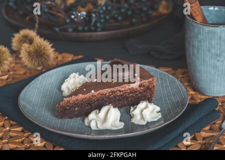 Stück hausgemachte Schokoladenkuchen mit Creme auf einem grauen Teller auf einem herbstlich dekorierten Tisch. Stockfoto