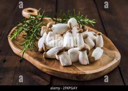 Rohe Königsausternpilze und Rosmär auf einem Holzbrett Stockfoto