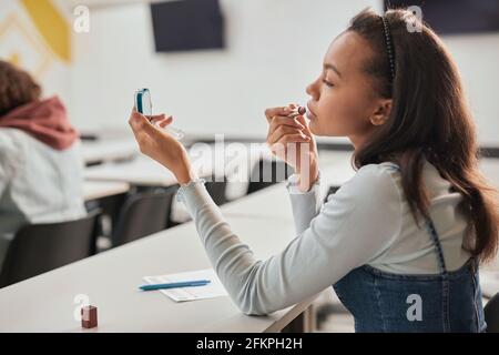 Seitenansicht Porträt von hübschen Teenager-Mädchen tun Make-up in der Schule Klassenzimmer und Blick in Spiegel, kopieren Raum Stockfoto