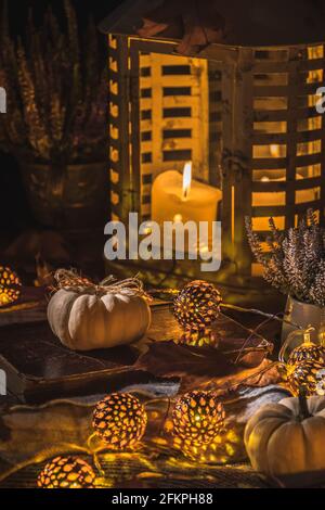 Herbstterrasse in der Nacht mit weißen Kürbissen, Lichtern und getrockneten Blättern, vertikales Stockfoto Stockfoto