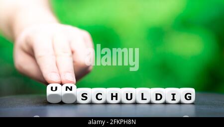 Hand dreht Würfel und ändert das deutsche Wort 'schuldig' (schuldig) in 'unschuldig' (Unschuld). Stockfoto