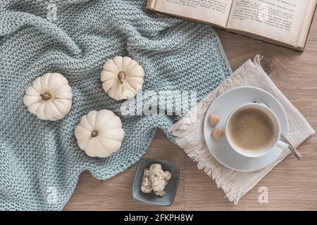 Konzept der gemütlichen Kaffeepause: tasse Kaffee, Wolldecke, weiße Mini-Kürbisse und ein altes Buch auf Eichenholzboden, Draufsicht Stockfoto