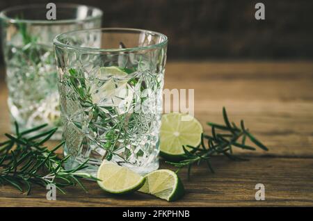 Gläser mit einem erfrischenden Limetten-Rosmarin-Getränk, Limettenhälften und Rosmarinzweigen auf altem Holz Stockfoto