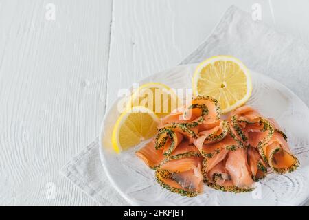 Geräucherte Lachsrollen mit Zitrone auf weißem Teller auf weißem Holzhintergrund, mit Kopierfläche Stockfoto