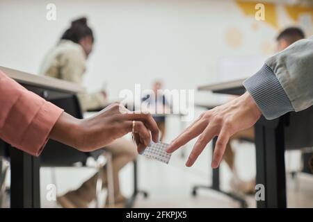 Nahaufnahme von zwei nicht erkennbaren Schülern, die beim Ablegen der Prüfung in der Schule eine Betrüger-Notiz übergeben, Platz kopieren Stockfoto