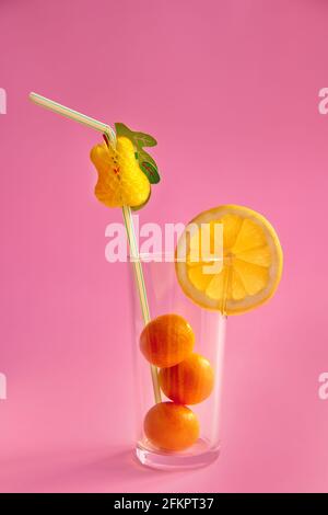 goldene Orangen - Kumquat mit einer Scheibe gelber Zitrone Glas mit Stroh auf rosa Hintergrund Stockfoto