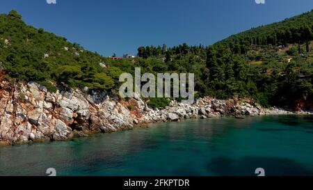 Luftdrohnen-Ansichten über eine felsige Küste, kristallklares ägäisches Meer, touristische Strände und viel Grün an einem wolkenlosen Tag in Skopelos isla Stockfoto