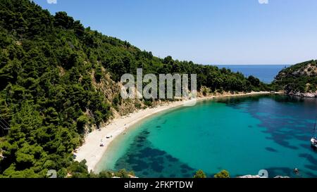 Luftdrohnen-Ansichten über eine felsige Küste, kristallklares ägäisches Meer, touristische Strände und viel Grün an einem wolkenlosen Tag in Skopelos isla Stockfoto