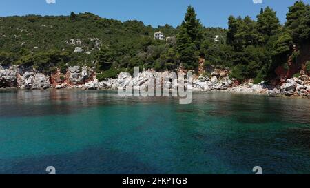 Luftdrohnen-Ansichten über eine felsige Küste, kristallklares ägäisches Meer, touristische Strände und viel Grün an einem wolkenlosen Tag in Skopelos isla Stockfoto