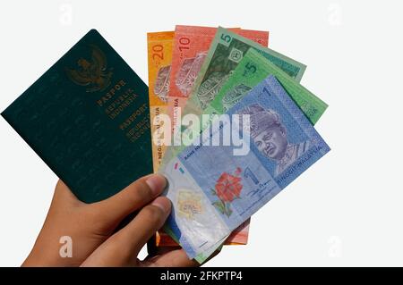 Hände mit Ringgit Malaysia Geld und einem indonesischen Passbuch, flacher Fokus und isoliert auf weißem Hintergrund. Das Konzept der Immigrant Employee Stockfoto