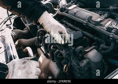 Automechaniker repariert einen Automotor. Die Hände des Mannes in Arbeitshandschuhen aus der Nähe. Diagnose und Wiederherstellung von Altteilen. Austausch von Hochspannungskabeln. Stockfoto