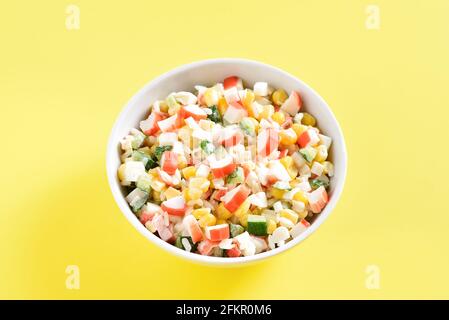 Nahaufnahme des nachgemachten Krabbensalats mit Krabbenstäbchen, Mais, Eiern, Gurke und Reis in Schüsseln auf gelbem Hintergrund. Stockfoto