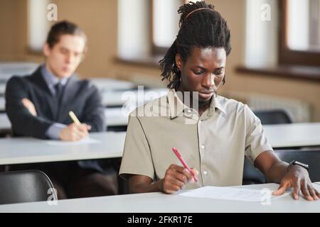 Porträt eines jungen afroamerikanischen Mannes, der in der Schule eine Prüfung ablegt, während er am Schreibtisch im College sitzt und denkt, Raum kopieren Stockfoto