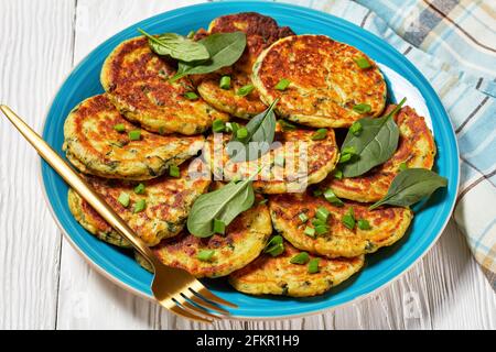 Kichererbsen-Spinat-Pfannkuchen auf einem blauen Teller mit goldener Gabel auf einem weißen Holztisch, Nahaufnahme Stockfoto