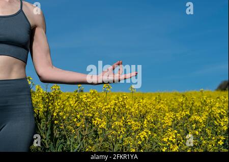 Nahaufnahme einer Frau, die in der Sonne auf einem gelben Rapsfeld meditiert und Yoga praktiziert. Stockfoto