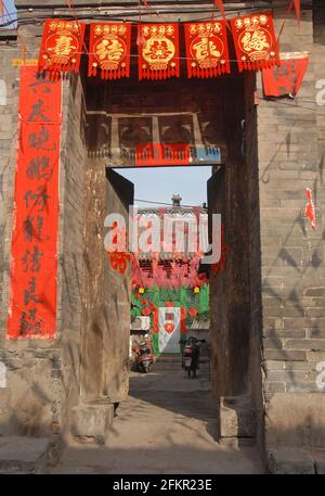 Blick in einen Innenhof in Pingyao, Provinz Shanxi, China, mit dem Eingang, der mit roten Spruchbändern und chinesischer Schrift geschmückt ist. Stockfoto