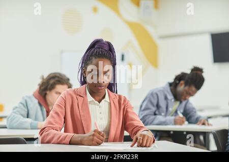 Eine vielfältige Gruppe von Studenten, die in der Schulklasse studieren, mit Schwerpunkt auf der jungen afroamerikanischen Frau, die vor dem Schreibtisch sitzt und Platz für Kopien hat Stockfoto