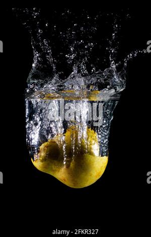 Der senkrechte Schuss der Birne im Wasser mit den Spritzern auf Ein dunkler, isolierter Hintergrund Stockfoto