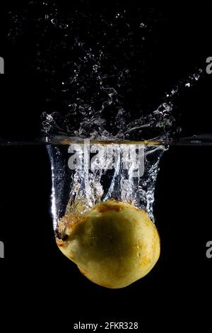 Der senkrechte Schuss der Birne im Wasser mit den Spritzern auf Ein dunkler, isolierter Hintergrund Stockfoto