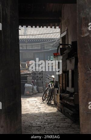 Pingyao in der Provinz Shanxi, China: Blick durch eine Tür in eine Gasse und einen Innenhof mit Fahrrädern Stockfoto