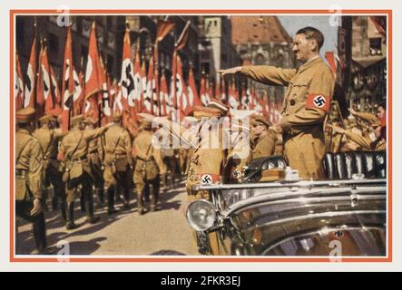 Adolf Hitler salutiert SA-Truppen Vintage Nazi Deutschland um 1935. Nürnberger Rallye, farbige Fotokarte von Adolf Hitler mit Hakenkreuzarmband in offenen Mercedes- und SA-Truppen, die mit Hakenkreuzfahnen vorbeimarschieren, Verlag H. Wiedemann, Sturmabteilung die offizielle Uniform der SA war das braune Hemd mit brauner Krawatte, bekannt als „die braunen Shirts“. Stockfoto