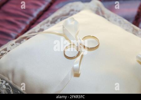 Goldene und silberne Ringe, die mit einer Schleife an ein Kissen gebunden sind. Stockfoto