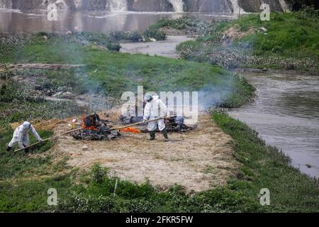 Kathmandu, Nepal. Mai 2021. Nepalesische Männer werden mit persönlicher Schutzausrüstung (PSA) gesehen und äschern die Leichen eines COVID-19-Opfers am Ufer des Bagmati-Flusses ein. Die nepalesische Regierung Verbot alle nationalen und internationalen Flüge bis zum 14. Mai 2021, da die Zahl der COVID-19-Fälle im Land weiter ansteigt. Kredit: SOPA Images Limited/Alamy Live Nachrichten Stockfoto