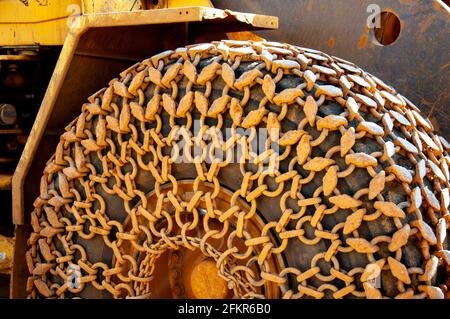 Grobkörnige Ketten in der Nähe anschoben. Schwere Metallketten, die mit gelbem Sand auf einem riesigen Reifen der Baumaschine verschmutzt sind. Ketten mit Kettengliedern aus der Nähe. Kontra Stockfoto