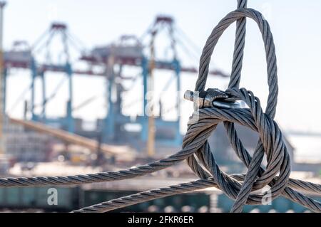 Verdrehter Drahtseilknoten in Nahaufnahme mit verschwommener industrieller Landschaft des Hafenpiers im Hintergrund. TIS Frachtterminal im größten Hafen der Ukraine. Industrie Stockfoto