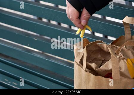Mann, der französische Pommes mit Fingern aus einem Papiersack auf einer Holzbank in Bern, Schweiz, isst. Stockfoto
