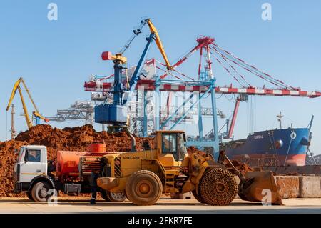 Containerterminal des Trockenfrachthafens der TIS Group. Bauwagen und schwere Bulldozer von Volvo am Hafenanlegeplatz mit festfahrendem Frachtschiff und Landkranen. Ad Stockfoto