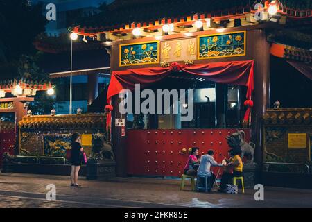 Chinatown, Singapur - 03. Januar 2015: Eine Frau betet vor einem buddhistischen Tempel, während eine kleine Gruppe von Frauen nachts in Singapur Karten spielt Stockfoto