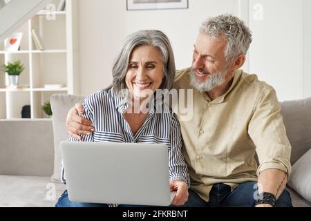 Glückliches, reifes Paar im mittleren Alter, das zu Hause mit einem Laptop E-Commerce-Shopping macht. Stockfoto
