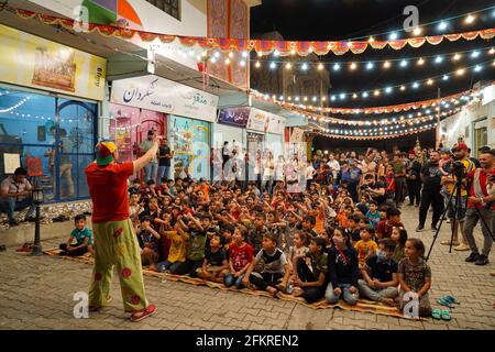 Iraqi Children interagieren mit einem italienischen Clown, der eine Unterhaltungsshow für sie vorführt.eine Unterhaltungsshow wird vom italienischen Clown Marco Rodari inszeniert, Bekannt als Claun il Pimpa für Kinder in der Hammam Al-Manqusha-Gegend in der Altstadt von Mossul, um ihnen zu helfen, mit den Auswirkungen des Krieges und der Besetzung der Stadt durch den IS (Islamischer Staat des Irak und Syrien) fertig zu werden. Die Show fand in dieser fröhlichen blauen Gasse statt, die vor kurzem von Jugendlichen Freiwilligen neu organisiert und arrangiert wurde, um eine wunderschöne Fassade des Gebiets zu werden, das sich nach der Zerstörung durch den letzten Krieg erholt hat. Stockfoto