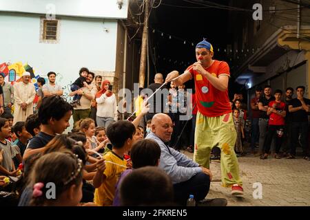 Iraqi Children interagieren mit einem italienischen Clown, der eine Unterhaltungsshow für sie vorführt.eine Unterhaltungsshow wird vom italienischen Clown Marco Rodari inszeniert, Bekannt als Claun il Pimpa für Kinder in der Hammam Al-Manqusha-Gegend in der Altstadt von Mossul, um ihnen zu helfen, mit den Auswirkungen des Krieges und der Besetzung der Stadt durch den IS (Islamischer Staat des Irak und Syrien) fertig zu werden. Die Show fand in dieser fröhlichen blauen Gasse statt, die vor kurzem von Jugendlichen Freiwilligen neu organisiert und arrangiert wurde, um eine wunderschöne Fassade des Gebiets zu werden, das sich nach der Zerstörung durch den letzten Krieg erholt hat. Stockfoto