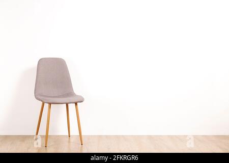 Ein eleganter grauer Loft-Stuhl, der allein auf Holzboden in einem leeren Raum steht, großer, weißer Wandhintergrund. Großer Kopierbereich für Text. Nur ein Vaca Stockfoto