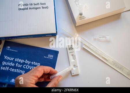Inhalt des NHS Covid-19 Rapid-Antigen-Selbsttestkits; eine Frau, die Testflüssigkeit auf die Antigentestkassette tropft. Stockfoto