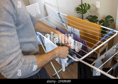 Ein Mann legt die gewaschenen Kleider auf den Trockner, der sich in einem Zimmer in der Wohnung befindet. Hygienekonzept, Männer zu Frauen im Haus zu helfen, sich zu verändern Stockfoto