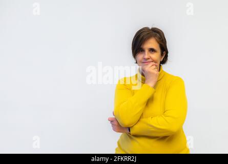 Weiße kaukasische Frau mittleren Alters in gelbem Pullover in nachdenklicher Pose Mit Armen und Kopf auf weißem Hintergrund selektiver Fokus und Speicherplatz kopieren Stockfoto