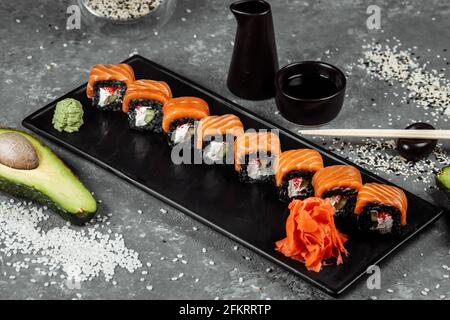 Eine Reihe von Sushi-Rollen Philadelphia mit rotem Fisch, Frischkäse und schwarzem Rise liegt auf einem Teller Boot. Sushi rollt auf grauem Hintergrund Stockfoto