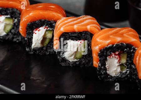 Eine Reihe von Sushi-Rollen Philadelphia mit rotem Fisch, Frischkäse und schwarzem Rise liegt auf einem Teller Boot. Sushi rollt auf grauem Hintergrund Stockfoto