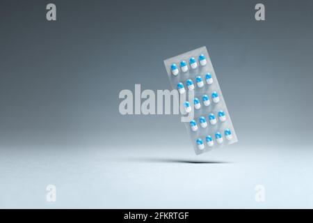 Blaue und weiße Pillen in einer Blisterpackung, die über einem nahtlosen Hintergrund schwebt. Apothekenkonzept. Stockfoto