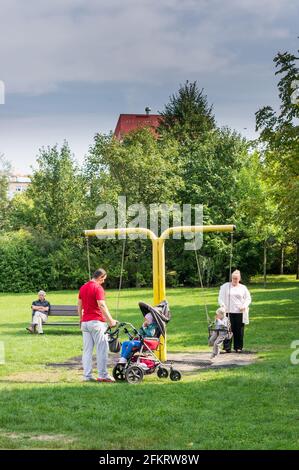 POZNAN, POLEN - 11. Sep 2017: Mann und Frau mit zwei Kindern, darunter ein Kind, das in einem Buggy durch eine Schaukel auf einem Spielplatz behindert ist. Stockfoto