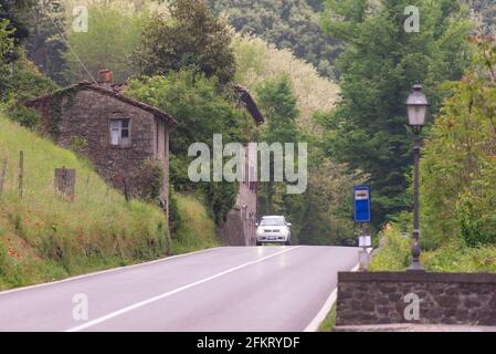 Die Straße in den Ausläufern der Toskana. Alte Steinhäuser entlang der Straße in den Bergen. Ein einbahntes Auto auf der Straße. Stockfoto