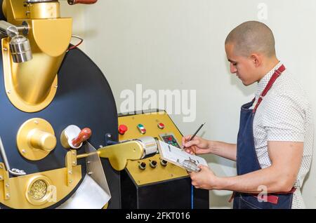 Hände des Mannes rösten Kaffee aromatische Kaffeebohnen über eine moderne Maschine zum Rösten von Bohnen. Stockfoto