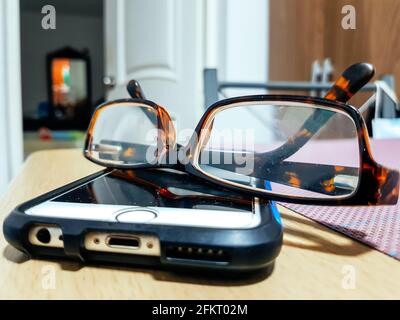 Brille mit Handy auf Holztisch in der Nacht, Nahaufnahme. Stockfoto