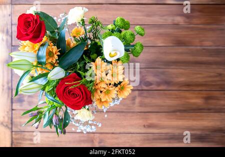 Draufsicht auf einen Strauß aus verschiedenen Blumen mit Rosen, Calla-Lilien, Gänseblümchen und Nelken, auf einem Holztisch unscharf, selektiver Fokus auf den bou Stockfoto